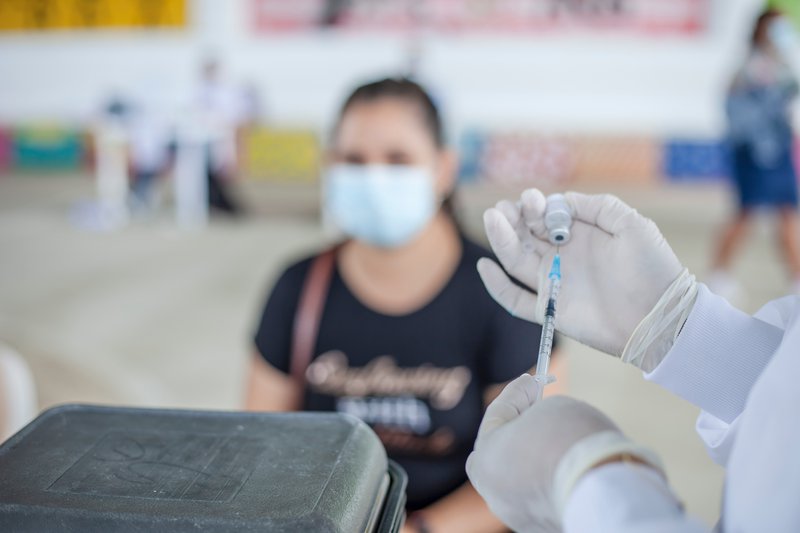 Nurse with a vaccine and a woman wearing a mask in the background