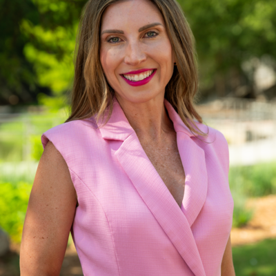 A woman with long hair smiling and wearing a sleeveless pink blazer.
